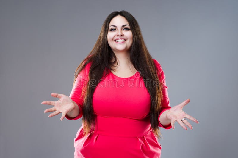 Modelo moreno feliz del tamaño extra grande en el vestido rojo, mujer gorda con el pelo largo en el fondo gris, concepto positivo imagenes de archivo Modelo moreno feliz del tamaño extra grande en el vestido rojo, mujer gorda con el pelo largo en el fondo gris, concepto positivo imagenes de archivo
