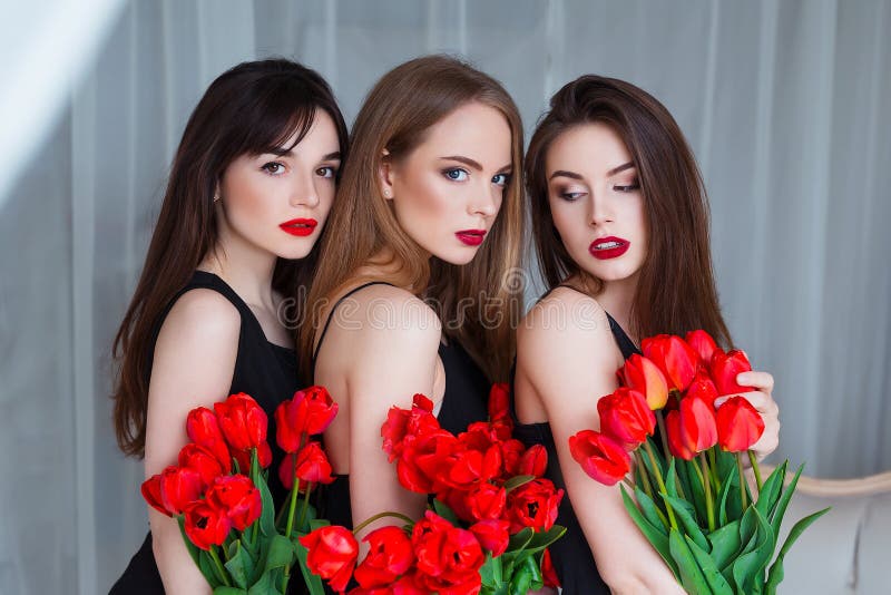 Modelos de moda en los vestidos negros blandos que presentan de manera sensual en el interior de lujo por completo de tulipanes S foto de archivo libre de regalías Modelos de moda en los vestidos negros blandos que presentan de manera sensual en el interior de lujo por completo de tulipanes S foto de archivo libre de regalías