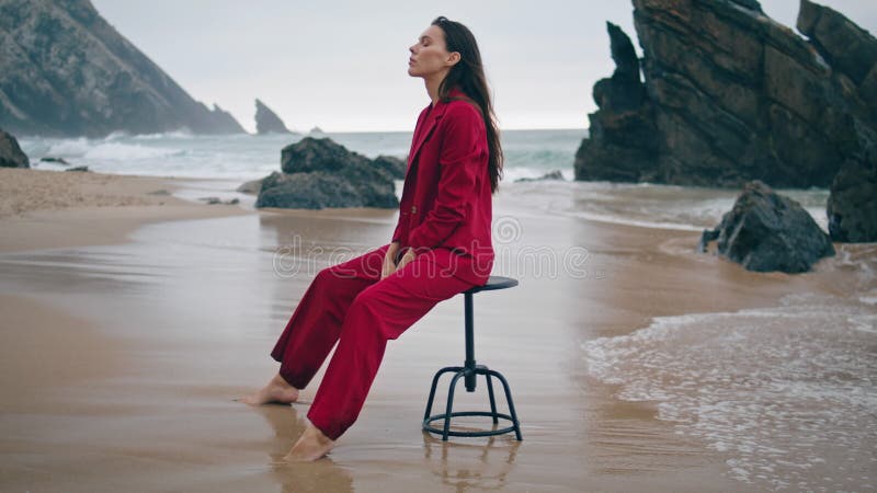 Modemeisje dat strandt in een rode elegant pak overdag. zittende vrouw.