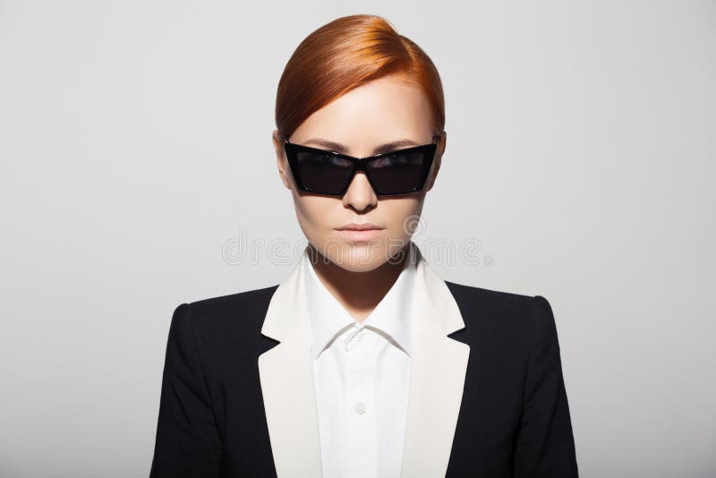 Fashion portrait of serious woman dressed as a secret agent or spy. Gray background. Fashion portrait of serious woman dressed as a secret agent or spy. Gray background.