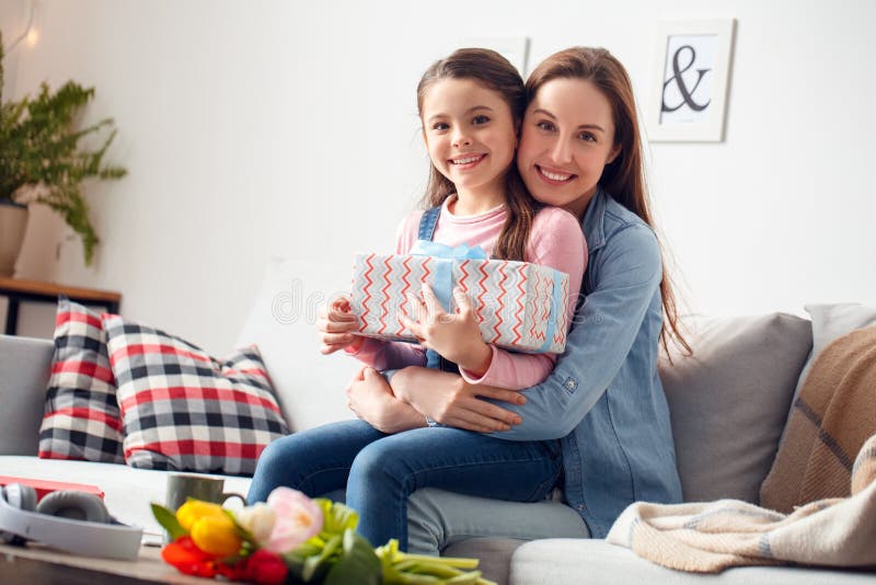 Moder för hemmastadd födelsedag för moder som och för dotter sittande kramar att le för ask för dotterinnehavgåva som är lyckligt fotografering för bildbyråer Moder för hemmastadd födelsedag för moder som och för dotter sittande kramar att le för ask för dotterinnehavgåva som är lyckligt fotografering för bildbyråer