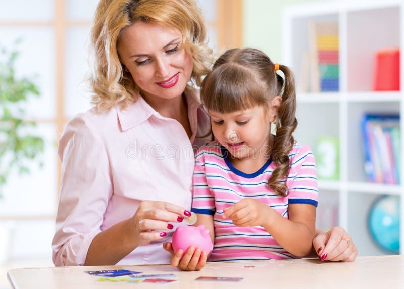 Moder och dotter som sätter mynt in i den piggy gruppen arkivbild Moder och dotter som sätter mynt in i den piggy gruppen arkivbild