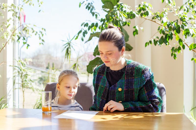 Focused mother helps her young daughter read menu at sunny wooden table, surrounded by lush indoor plants in a cozy setting. Focused mother helps her young daughter read menu at sunny wooden table, surrounded by lush indoor plants in a cozy setting
