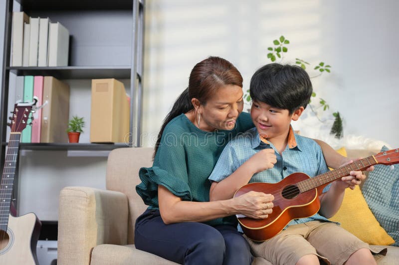 Moder och son Enjoying Ukulele Music Together at Home Asian Woman Teaching Kid Boy to Play Ukulele in Living Room royaltyfri foto