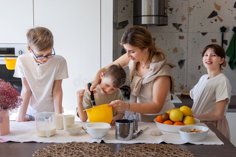 Moder som hjälper son att stöta på bakblandning. Glad mamma hjälper unga människor att blanda batter i köket medan syskon tittar arkivbild