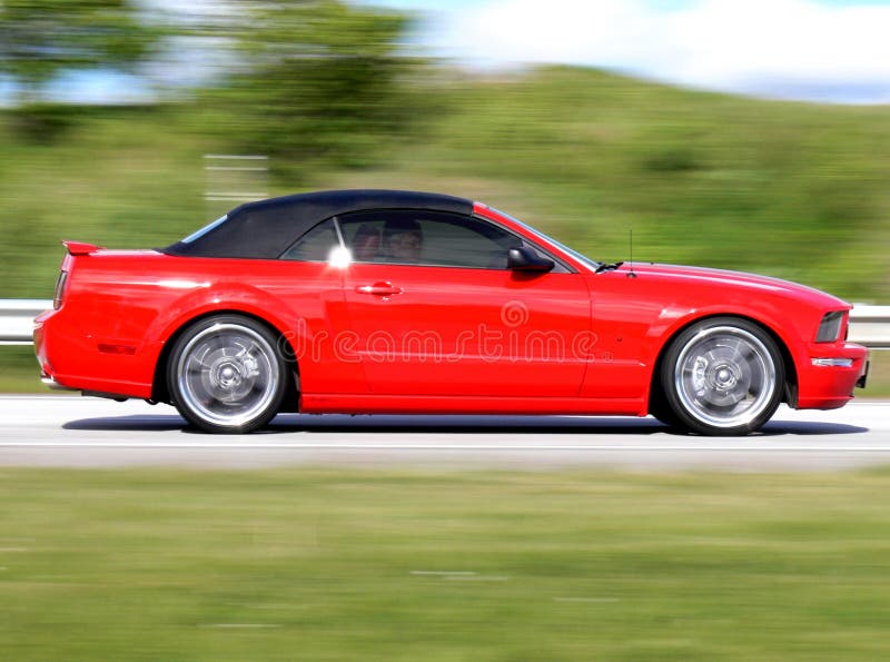 A modern red american convertible speeding by on the road. A modern red american convertible speeding by on the road