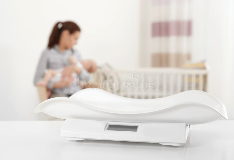 Modern baby scales on table and blurred woman with child indoors royalty free stock image Modern baby scales on table and blurred woman with child indoors royalty free stock image