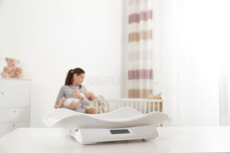 Modern baby scales on table and blurred woman with child indoors royalty free stock photography Modern baby scales on table and blurred woman with child indoors royalty free stock photography