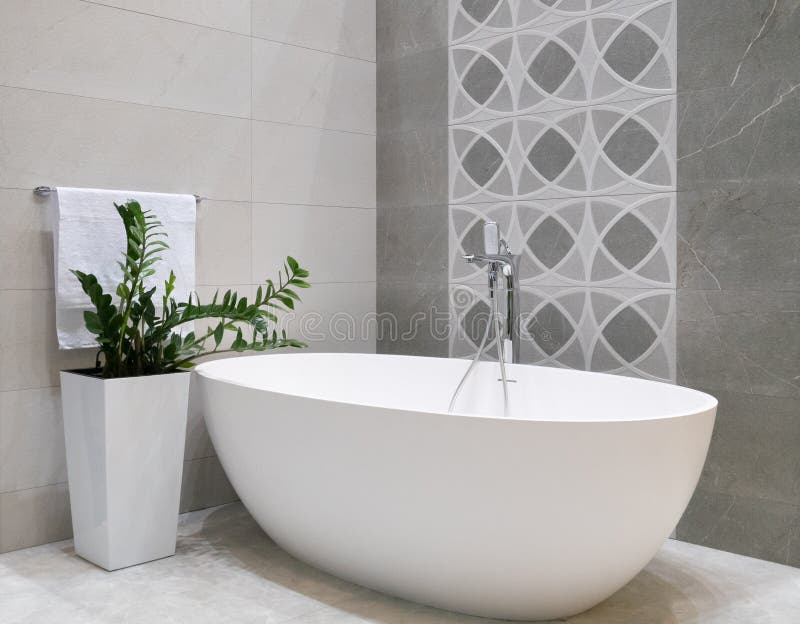 Modern badruminredesign med vitstenbadkaret, den gråa tegelplattaväggen, den keramiska blomkrukan med den gröna växten och h