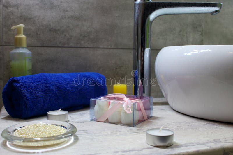 Modern bathroom design with white washbasin and metal crane and decoration. Blue towel and candles and cosmetics against grey wall royalty free stock photography Modern bathroom design with white washbasin and metal crane and decoration. Blue towel and candles and cosmetics against grey wall royalty free stock photography