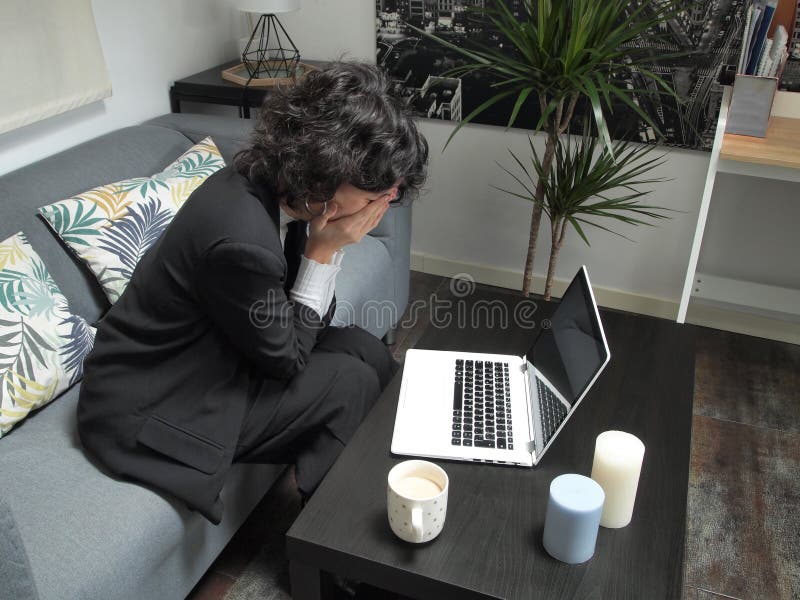 Modern business caucasian woman frustrated, crying, sitting on the sofa with a laptop and a cup of coffee royalty free stock image Modern business caucasian woman frustrated, crying, sitting on the sofa with a laptop and a cup of coffee royalty free stock image