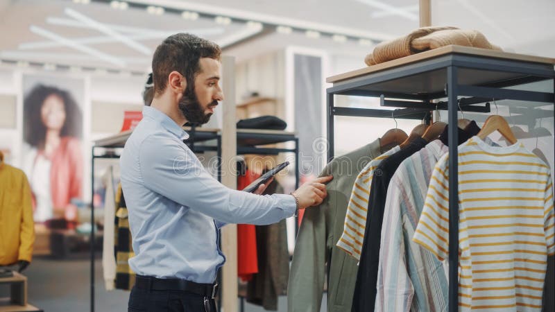Magazin de îmbrăcăminte modern : bărbat vizual merchandising profesional utilizează un computer tabletă digital pentru a crea stock photo
