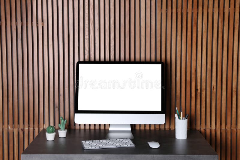 Modern computer monitor on desk against wooden wall
