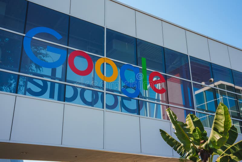 Colorful Google logo on modern corporate building with lush green leaves in foreground. stock image