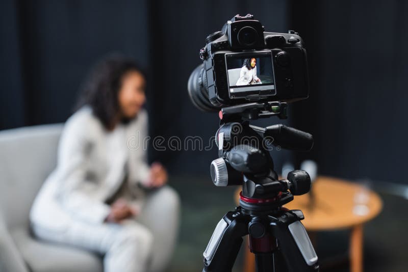 Modern digital camera on tripod with. African american journalist sitting in armchair on screen,stock image