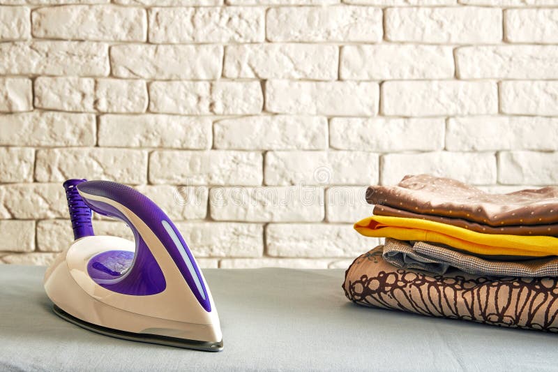 Modern Electric Iron on an Ironing Board with a Stack of Ironed Clothes