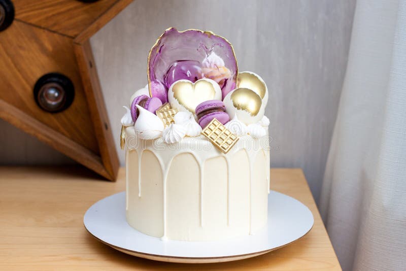 Modern elegant cake with melted white chocolate, golden heart and chocolate balls, macaroons, meringue and caramel.