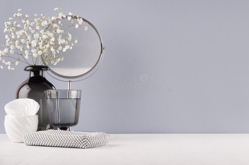 Modern elegant female dressing table with black glass vase with flowers, mirror, silver cosmetic bag on grey color wall and white.