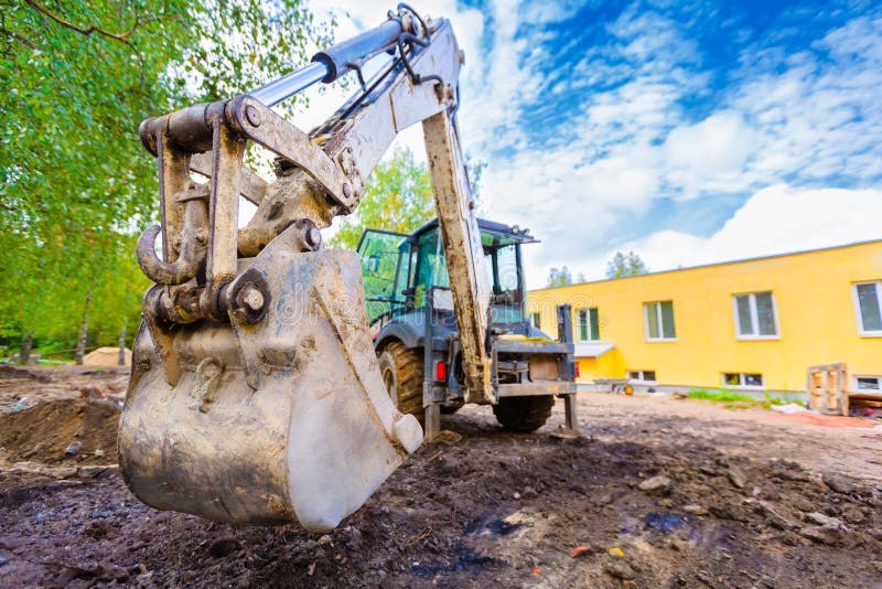 The modern excavator performs excavation work on the construction site. Front view of a digger bucket of digging ground