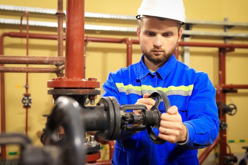 Modern industrial machine operator working in heating station. Worker turns gate valve of pipeline. Man in workwear closes valve royalty free stock photography Modern industrial machine operator working in heating station. Worker turns gate valve of pipeline. Man in workwear closes valve royalty free stock photography