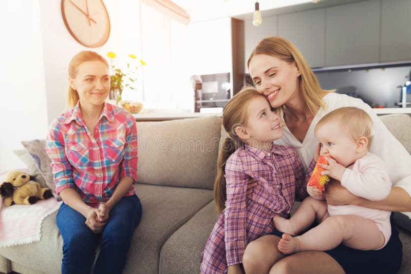 Modern med älskvärda ungar sitter på soffan nära barnflicka royaltyfri foto Modern med älskvärda ungar sitter på soffan nära barnflicka royaltyfri foto