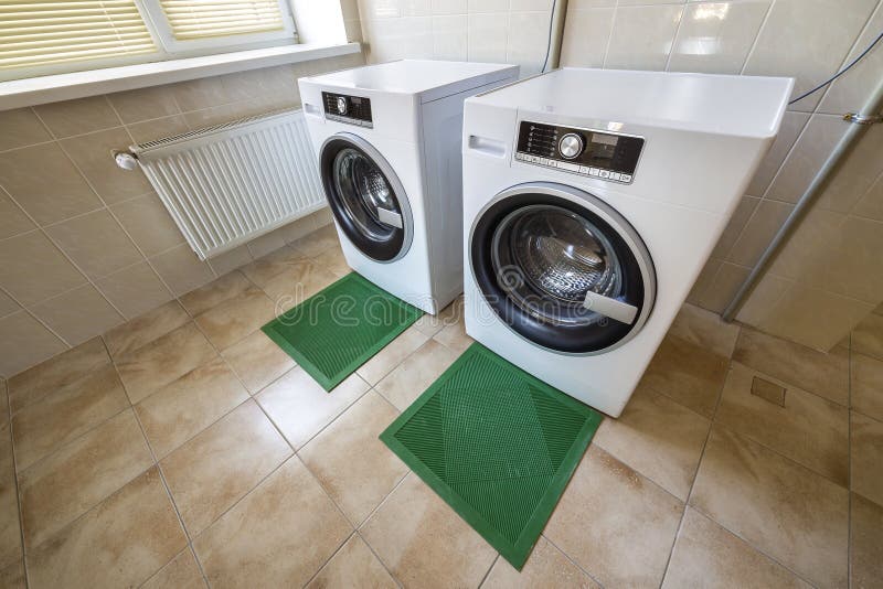 Modern new industrial washing machines in clean tiled bathroom or laundry room on rubber insulation mats.