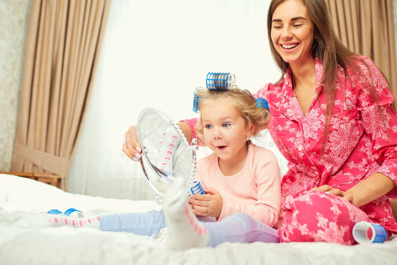 Modern och dottern i pyjamas spelar med en spegel tillsammans royaltyfri bild Modern och dottern i pyjamas spelar med en spegel tillsammans royaltyfri bild
