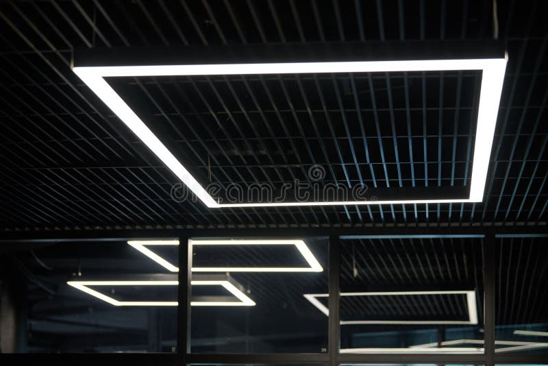 Modern office lighting. Thin lamps in office dark ceiling. LED white cold light over workplaces