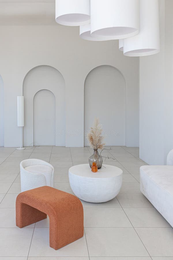 Modern pure white interior design of a sprsious sitting room with soft stylish furniture. Large windows frame creating a serene atmosphere during daylight