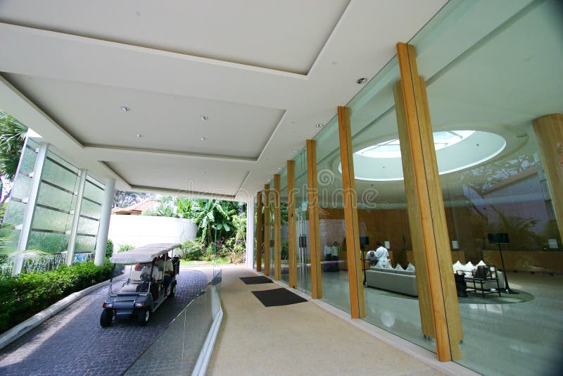 An exterior shot of a brand new modern five star holiday resort hotel on Sentosa island of Singapore. Cool contemporary architecture of glass, wood and steel combined with lush tropical landscaping for the exotic vacation mood. With a man-made waterfall feature on the left of the drive way. Small and light club car with canvas roof is used to ferry guests around the resort. Taken on a sunny day in bright sunlight, with a wide angle lens for a dramatic view. Man made waterfall stock images, royalty-free photos and pictures