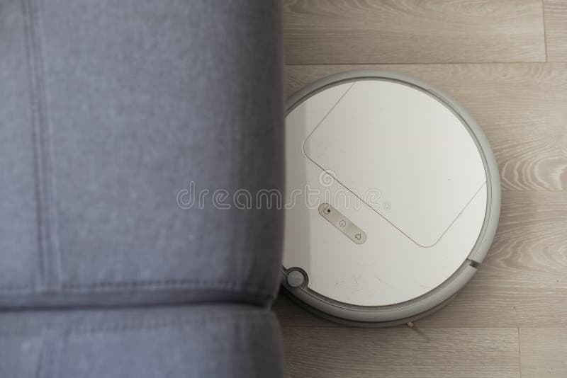 Modern Robot Vacuum Cleaner Near Sofa with Resting Woman in Room. Stock