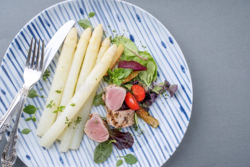 Modern skivad fläskfilé med vit sparris och rostpotatis på en designplatta royaltyfri bild