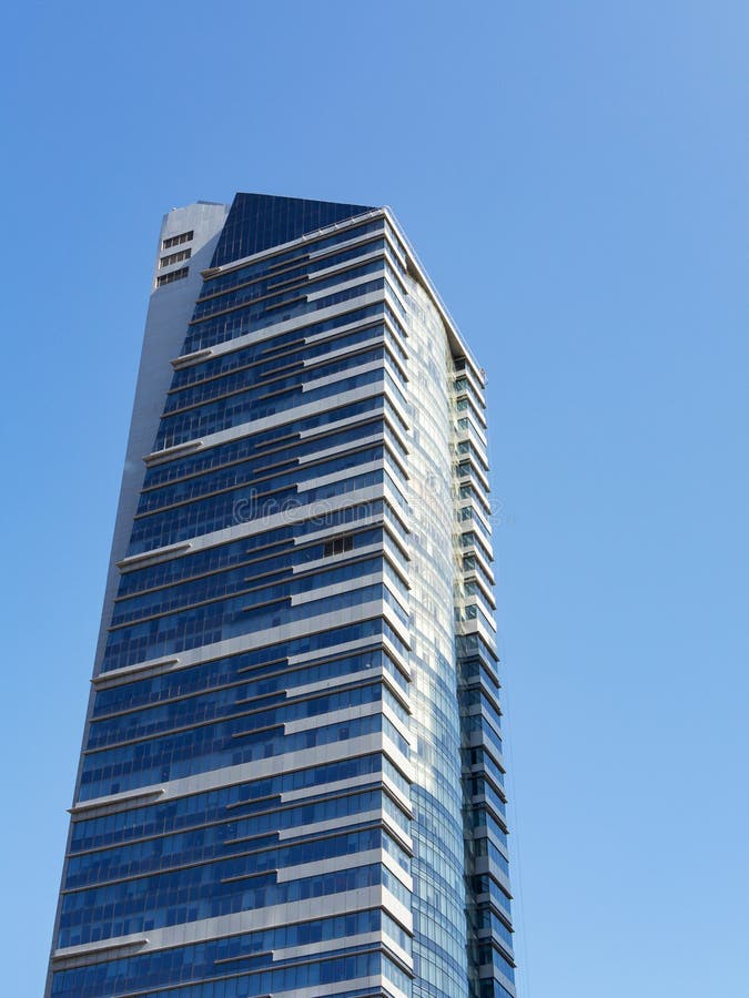 Modern skyscraper with glass facade and white stripes against blue sky, vertical
