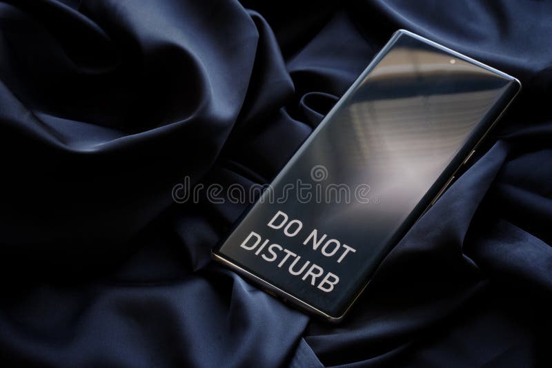 Modern smartphone with the inscription do not disturb on a dark background of cozy fabric. The concept of relaxation, solitude and