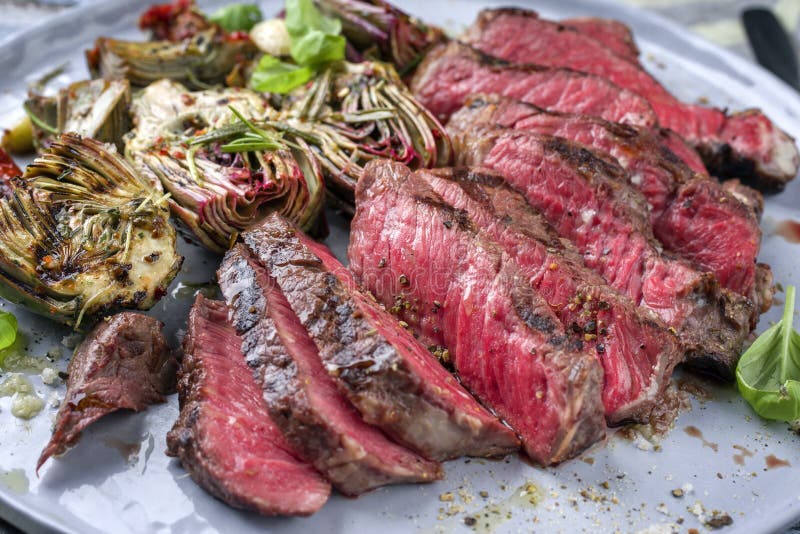 Modern style traditional barbecue angus entrecote beef steak with artichoke hearts and herbs on a Nordic design plate