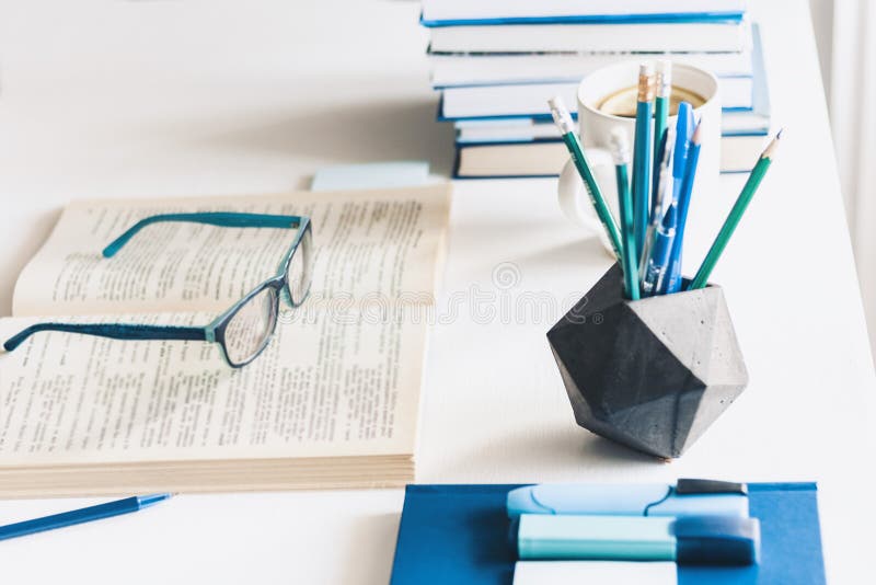 Modern stylish office work place with open book, glasses, office supplies and books, desk work concept in white and blue colors