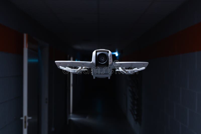 A modern surveillance drone with a camera flies through a dark, futuristic corridor, representing security technology and robotics stock photo