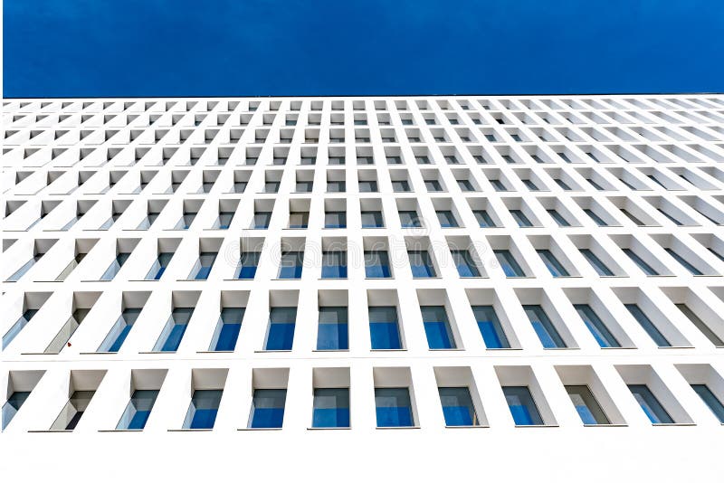 Modern tertiary and businness building with white facade and windows that reflect the blue sky