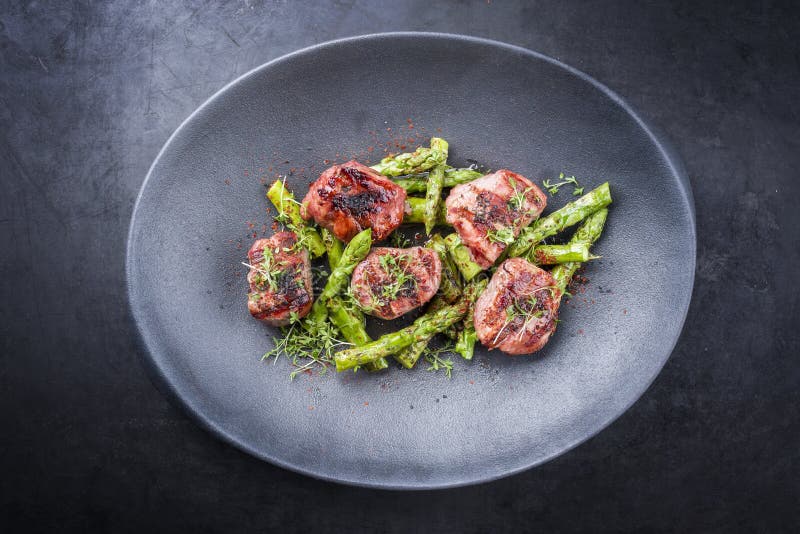 Modern traditionell barbecue iberiska porkfilémedaillon med gröna sparrspetsar på en designplatta arkivfoton