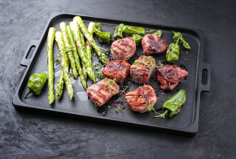 Modern traditionell barbecue iberiska porkfilémedaljoner med grön sparris och chili på en formgiven gjutjärnsbricka royaltyfri foto
