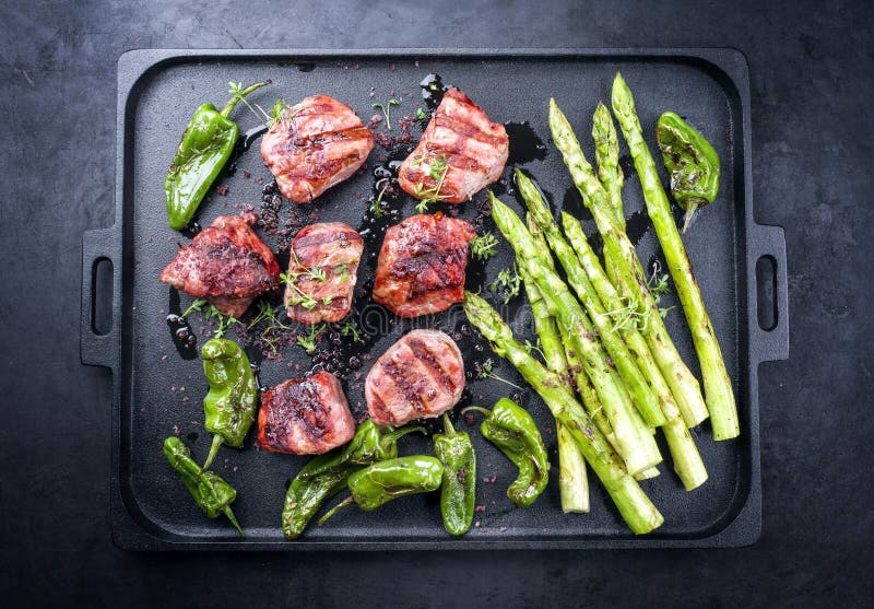 Modern traditionell barbecue iberiska porkfilémedaljoner med grön sparris och chili på en formgiven gjutjärnsbricka royaltyfri foto
