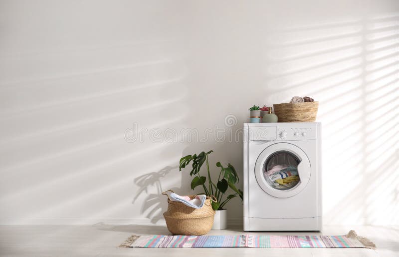 Modern washing machine and wicker basket with laundry near wall, space for text. Interior design stock photography