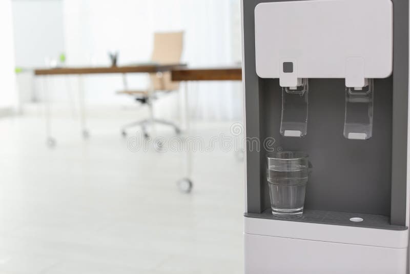 Modern Water Cooler with Glass in Office, Closeup. Stock Photo Image
