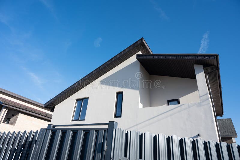 Modern white house with dark gray roof and fence under blue sky royalty free stock images