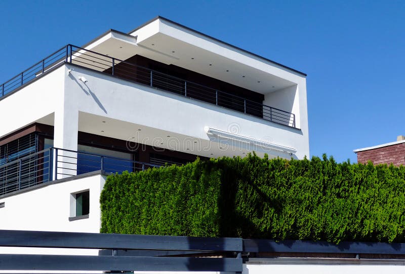 Modern white stucco cube shaped residential building with long balcony and evergreen hedge