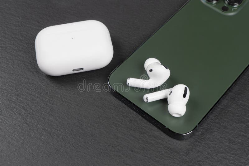 Modern wireless earbuds headphones with charging case and smartphone on stone table background.