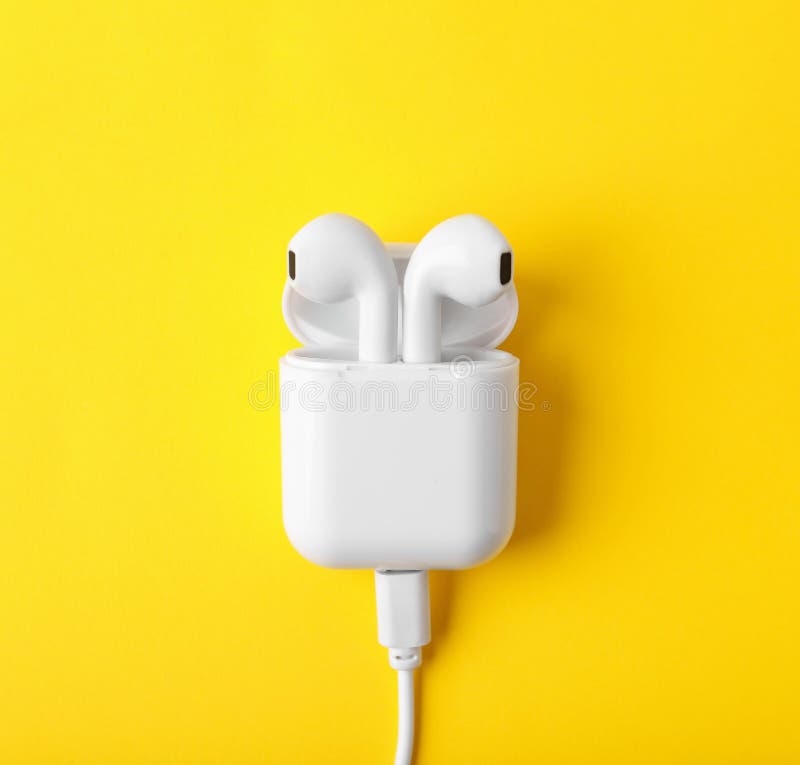 Modern wireless earphones in charging case with  on yellow background, top view