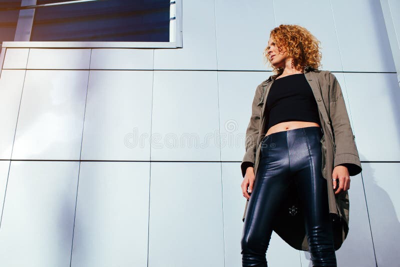 Moderne junge Frau mit dem roten gelockten Haar, das gegen graue Wand steht Vorbildliche tragende stilvolle Sommerausstattung der stockbild Moderne junge Frau mit dem roten gelockten Haar, das gegen graue Wand steht Vorbildliche tragende stilvolle Sommerausstattung der stockbild