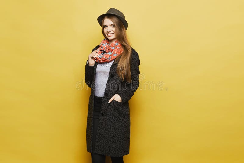 Fashionable and beautiful blonde model girl in stylish coat with leopard pattern, in trendy hat and in the colorful scarf posing at yellow background at a studio, isolated. Fashionable and beautiful blonde model girl in stylish coat with leopard pattern, in trendy hat and in the colorful scarf posing at yellow background at a studio, isolated.