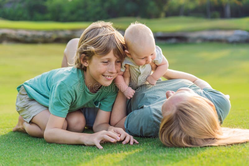 Moderäldre son och nyfödda barn på en ängsmark i parken. Familjeutgifter av hög kvalitet tillsammans i naturen. Parenthood royaltyfria foton